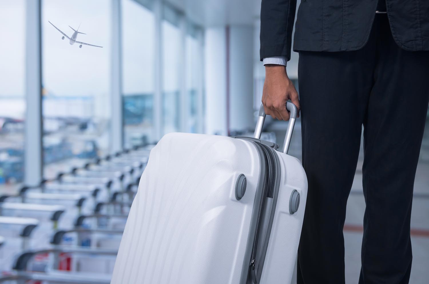 Businessman and suitcase in the airport departure lounge, airplane in the blurred background, summer vacation concept, traveler suitcases in airport terminal waiting area. .